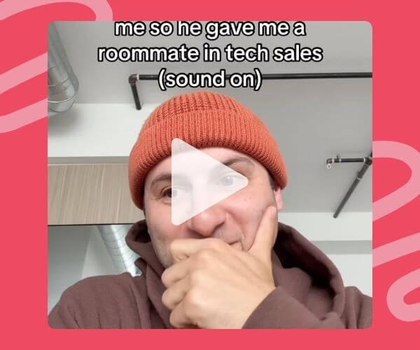 A man in a rust-colored beanie and brown hoodie sits with his hand over his mouth, looking amused. Text at the top says, “me so he gave me a roommate in tech sales (sound on)” with a play button overlay indicating it’s a video.
