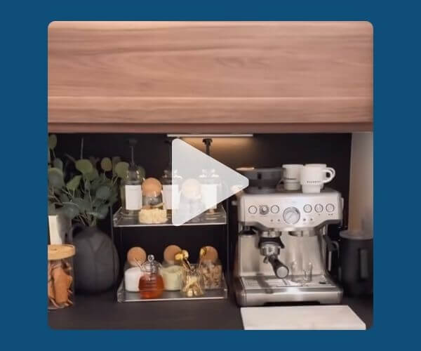 Aesthetic coffee station featuring a silver espresso machine, glass jars with ingredients, and neatly arranged mugs and decor, with a play button overlay centered on the image.