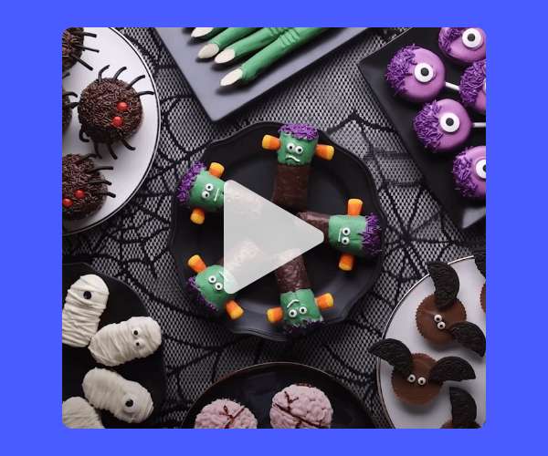 Overhead view of fun Halloween-themed treats on black plates, including spider cupcakes, Frankenstein Twinkies with candy arms, mummy cookies, purple monster cookies, and bat cupcakes, all arranged on a black web tablecloth.