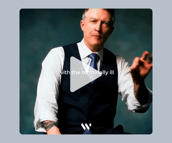 A man in a vest and tie speaks on camera against a dark teal backdrop, with a play button overlay and partially visible on-screen text reading “with the terminally ill.”
