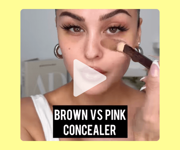 A woman applies brown concealer under her eye with a makeup brush in a close-up beauty tutorial labeled “Brown vs Pink Concealer.”