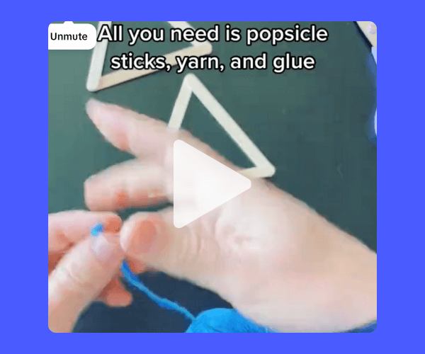 Hands are shown working with bright blue yarn over a dark tabletop, with popsicle sticks arranged in simple geometric shapes in the background. On-screen text reads: “All you need is popsicle sticks, yarn, and glue.”