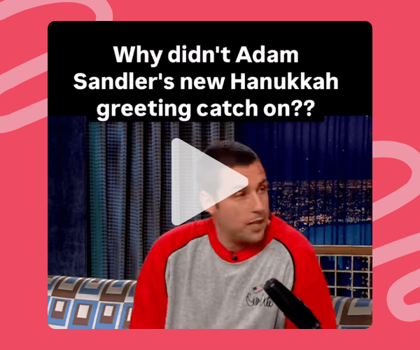 A video still shows Adam Sandler sitting on a late-night talk show set, with a cityscape backdrop and a bright pink border framing the clip. White text at the top reads, “Why didn’t Adam Sandler’s new Hanukkah greeting catch on??”