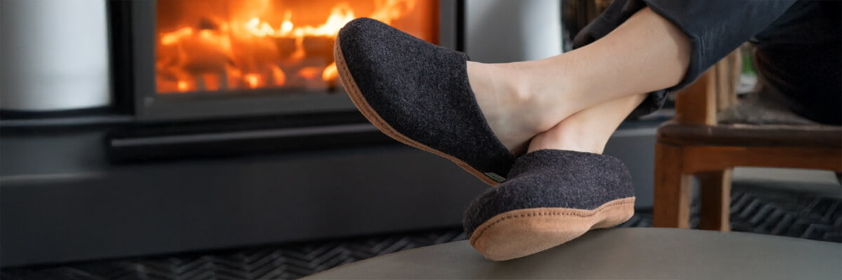 Someone lounges with their feet up in cozy dark slippers while a fireplace glows warmly in the background. It gives total “winter weekend relaxation” vibes.