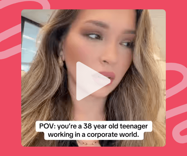 A woman with long highlighted hair looks off to the side in a car, with a play button overlay centered on the video. Text reads, “POV: you’re a 38 year old teenager working in a corporate world,” set against a red patterned background.