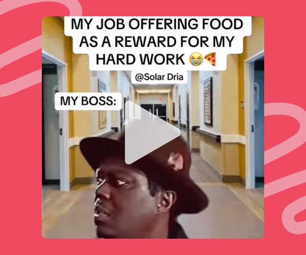 Meme-style video still of a man in a wide-brim hat standing in a long, yellow-toned office hallway, looking unimpressed, with on-screen text joking about a job offering food instead of real rewards. The video sits inside a bright pink overlay background.