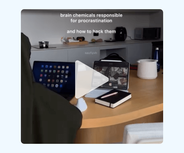A desk with multiple devices shows a laptop, tablet, and notebook while text mentions brain chemicals responsible for procrastination. The workspace looks tidy with shelves and tech in the background.