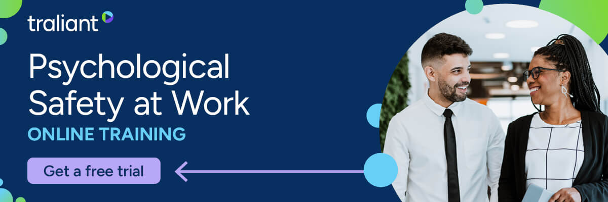 A dark blue banner promotes “Psychological Safety at Work” online training by Traliant, with a “Get a free trial” button. On the right, two coworkers smile at each other while walking through an office.