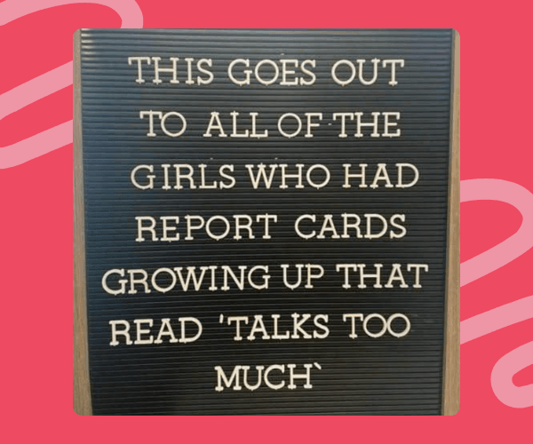 A black letter board with white plastic letters displays a full message, placed on a pink background with abstract shapes. The board is centered and fills most of the frame.