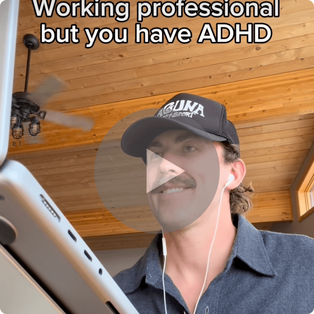 A man wearing a cap and earbuds looks at a screen while working indoors, with a play button overlay on the video. On-screen text reads, “Working professional but you have ADHD.”