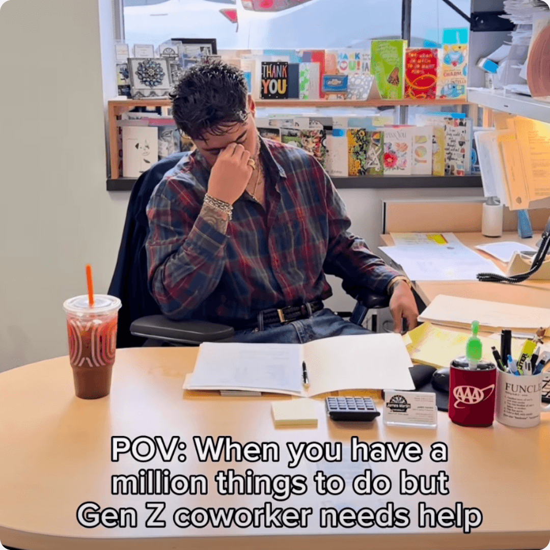 A meme shows a stressed man sitting at a cluttered office desk with paperwork and coffee around him. The caption says, “POV: When you have a million things to do but Gen Z coworker needs help.”