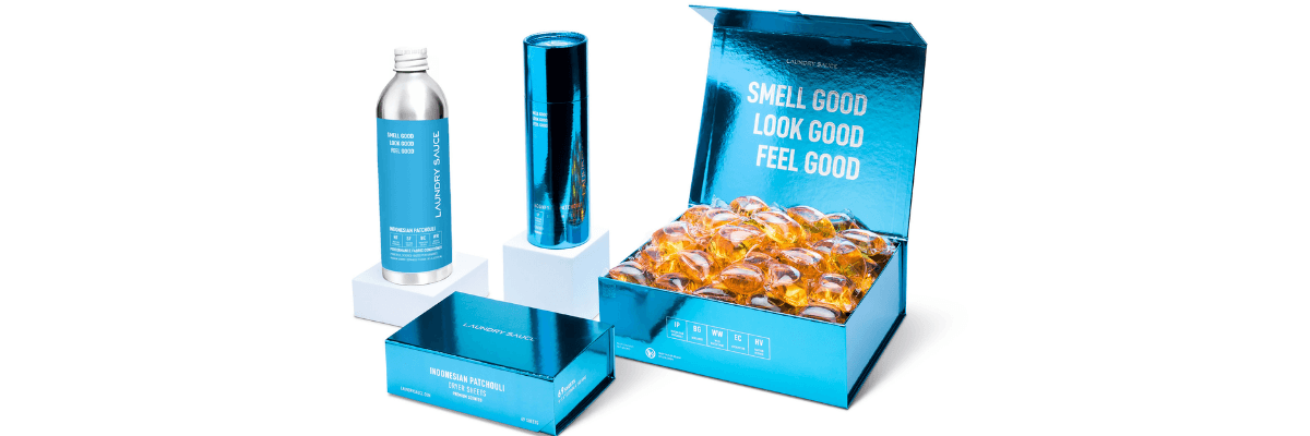 A Laundry Sauce product display features detergent products and scent pods arranged beside an open blue box. The packaging includes the phrase “Smell Good Look Good Feel Good.”