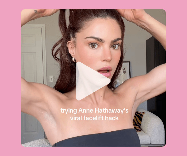 A woman with her hair tied in a high ponytail lifts her hair while facing the camera in a bright room. On-screen text says she is trying Anne Hathaway’s viral facelift hack.