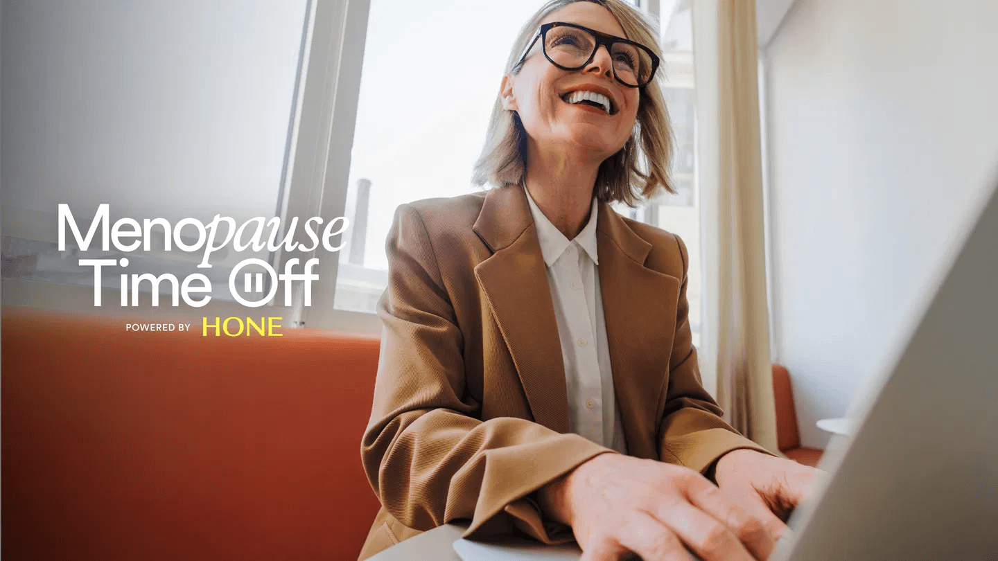 A promotional image shows a smiling woman wearing glasses and a tan blazer while working on a laptop in a bright office with large windows. White text on the left reads "Menopause Time Off," with smaller text below stating "Powered by HONE.”