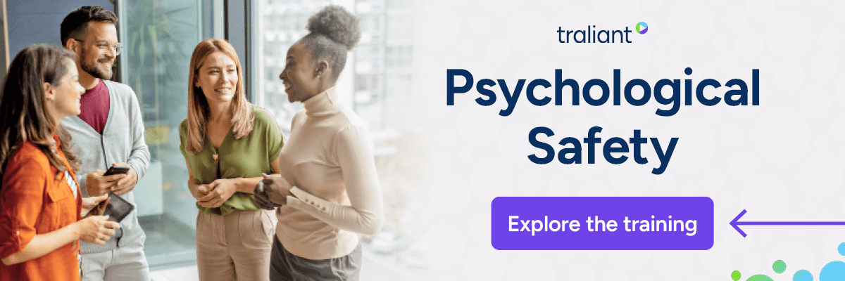 A group of four coworkers stand together in a bright office, smiling and talking near large windows. The right side features the Traliant logo, the headline “Psychological Safety,” and a purple “Explore the training” button.
