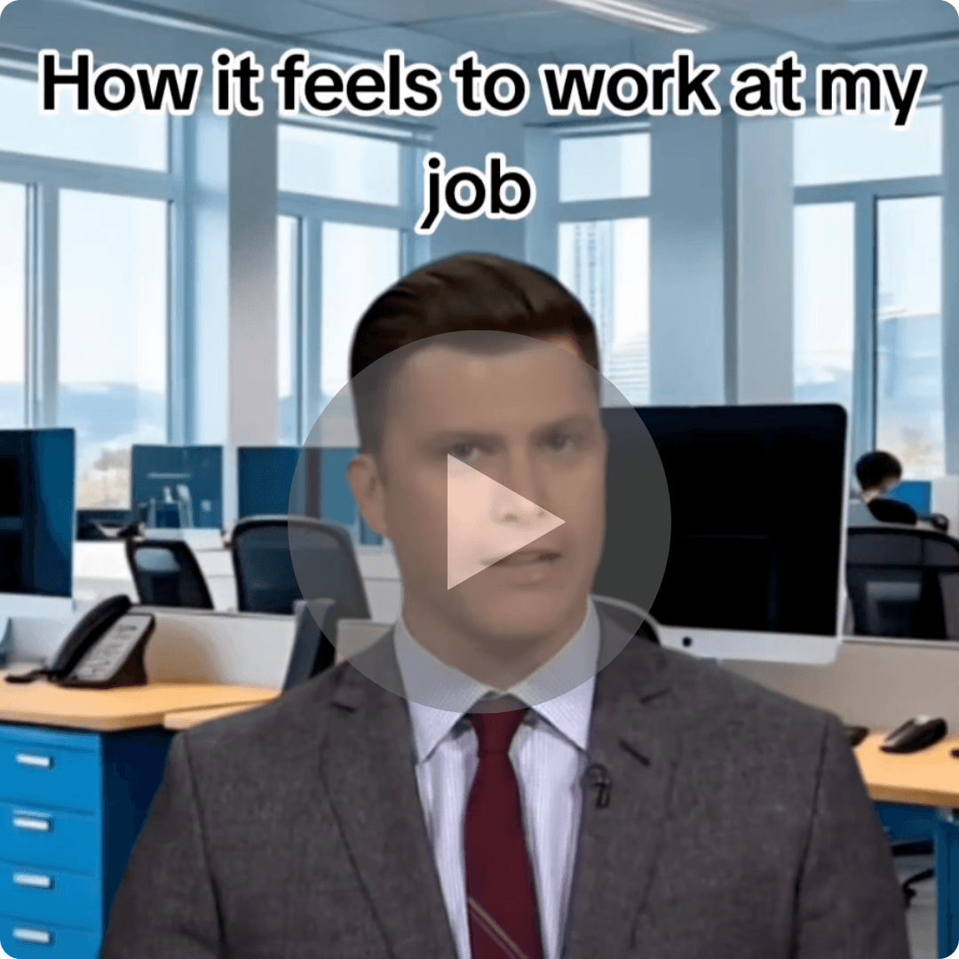 A man in a gray suit and red tie sits at a desk in a bright office with computer monitors and windows behind him. Large white text across the top reads, “How it feels to work at my job,” while a translucent play button covers the center of the image.