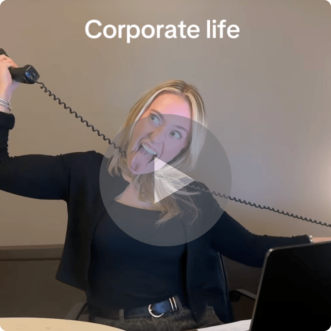A woman in an office holds a corded telephone receiver above her head while sticking out her tongue. Large white text at the top reads, “Corporate life,” and a laptop is visible in front of her.