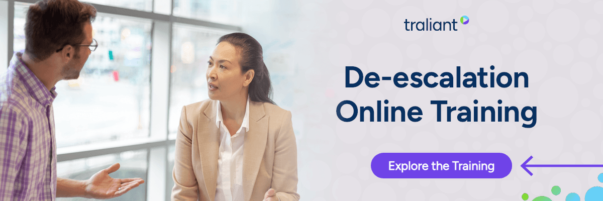 Two people are standing in a bright office-like space, facing each other and talking. A large text panel on the right reads “De-escalation Online Training,” with a purple button below.