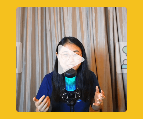 A woman with long black hair and glasses speaks into a glowing blue microphone in front of beige curtains, with a play button over the video.