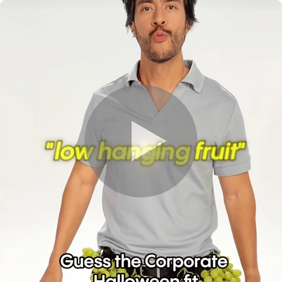 A man wearing a light gray polo shirt stands against a white background with green grapes around his waist. Yellow text reads “low hanging fruit,” with “Guess the Corporate Halloween fit” at the bottom.