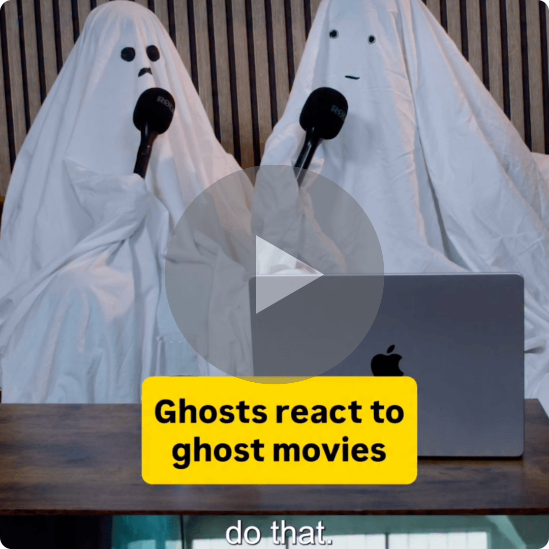 Two people dressed as white-sheet ghosts sit behind a laptop holding microphones. A yellow caption reads “Ghosts react to ghost movies.”
